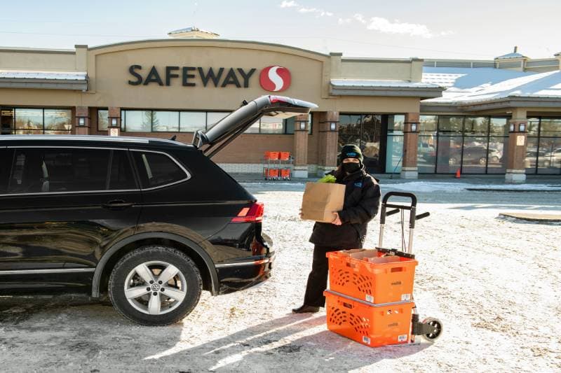 Voilà by Safeway teammate delivers grocery order in designated Safeway curbside pickup parking spot in Calgary, Alberta.