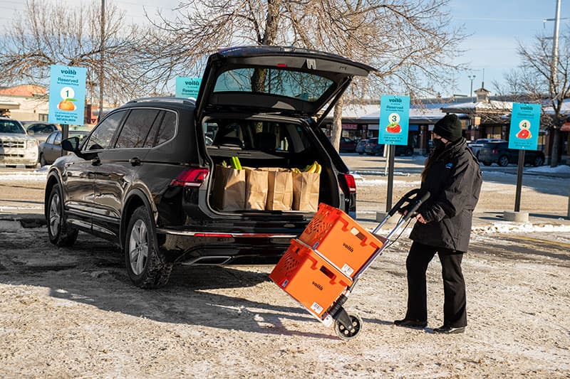 Voilà by Safeway teammate delivers grocery order in designated Safeway curbside pickup parking spot in Calgary, Alberta.